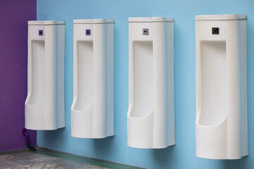 Four white urinals are mounted on a wall