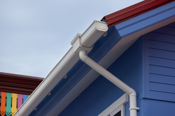 Naklejka premium A white pipe and rain gutter is attached to the roof of a blue house.