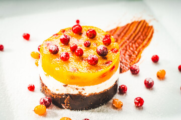 Dessert or cake in layers: yellow sea buckthorn and mango jelly with lingonberries, mascarpone and chocolate shortcrust pastry on a white plate, decorated with berries and chocolate sauce.