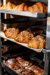 Close-up of freshly baked bread and croissants displayed on a rack in a bakery. Variety of baked goods