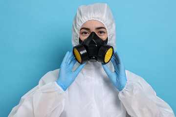 Worker in respirator and protective suit on light blue background
