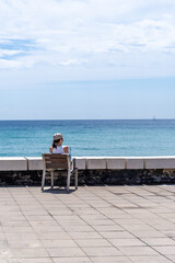 A person sits alone facing the expansive blue sea, evoking a sense of solitude and reflection.