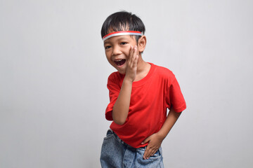 Cute Asian boy in red shirt makes a whispering gesture with his hands, isolated on white background. Indonesian Independence Day concept.
