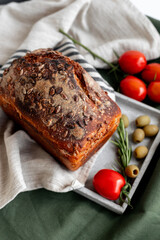 An exquisitely sliced artisan bread loaf is beautifully arranged alongside juicy tomatoes and olives on rustic fabric