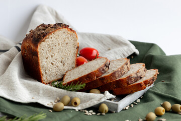 An exquisitely sliced artisan bread loaf is beautifully arranged alongside juicy tomatoes and olives on rustic fabric