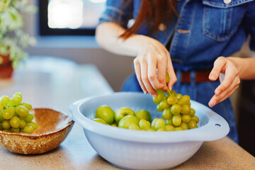 Woman picking green grapes from bowl on kitchen counter in sunny morning light