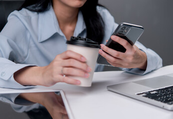 businesswoman holding a coffee cup and checking her smartphone, reflecting a moment of multitasking during a work break.