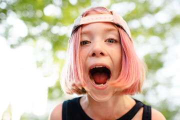 Stylish kid girl with blonde pink hairstyle pre teen age 9 -10 year old with open mouth wearing cap outdoor. Childhood