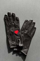 A pair of black, leather gloves with a red heart on the palm