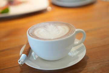 Hot latte art coffee in white ceramic cup on wooden table.
