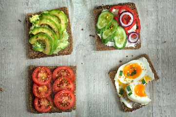 Four delicious sandwiches on whole grain rye bread with egg and various vegetables and seasonings. Top view