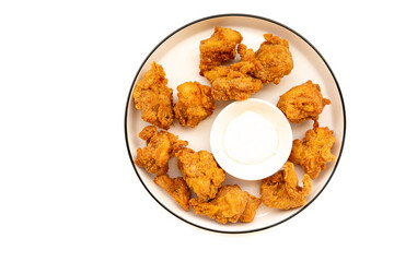 Crispy, golden-brown chicken nuggets arranged around a small white bowl of dipping sauce on a white plate with a dark rim. A classic and popular finger food.