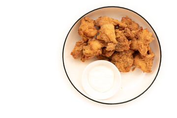 Crispy, golden-brown chicken nuggets arranged around a small white bowl of dipping sauce on a white plate with a dark rim. A classic and popular finger food.