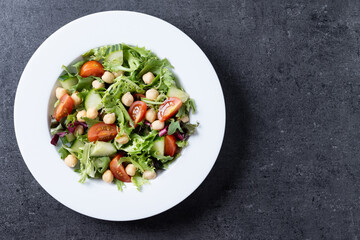Healthy chickpea salad with tomato,lettuce and cucumber on black slate background. Top view. Copy space