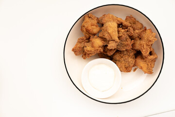 Crispy, golden-brown chicken nuggets arranged around a small white bowl of dipping sauce on a white plate with a dark rim. A classic and popular finger food.
