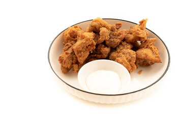 Crispy, golden-brown chicken nuggets arranged around a small white bowl of dipping sauce on a white plate with a dark rim. A classic and popular finger food.