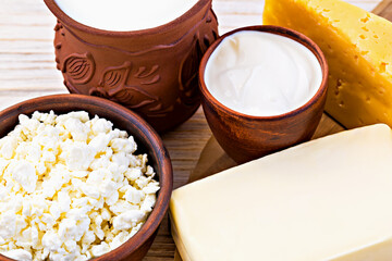 Assorted dairy products including butter, cheese and cottage cheese, sour cream and milk presented in traditional ceramic bowls on wooden surface, illustrating wholesome and nutritious selection