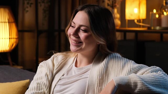 Portrait of a elegant, satisfied and confident Caucasian young woman sitting on sofa at evening home, looking at camera. Concept of people individuality.