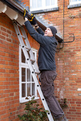 Man on a ladder fixing rain gutter on a UK house