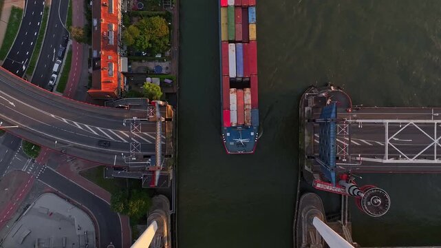 Top down view of a container barge sailing between an open bridge on a sunny evening.