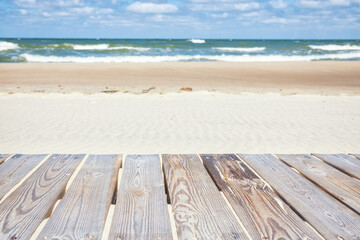 Close-up of wooden boards of a walkway on a beach. In the background you can see sand, sea with waves and sky with clouds. Landscape. Blank.