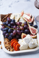 Variety of cheeses and fruits plate with wine, on white marble table.