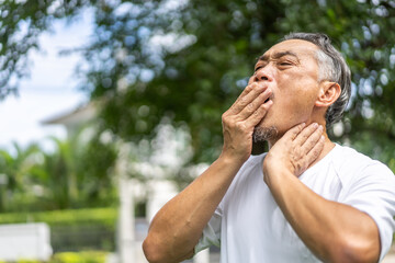 Senior asian man experiencing tooth pain, holding his cheek with pained expression, discomfort and common issues related to dental health, toothache, pain relief, and medical care for seniors at home