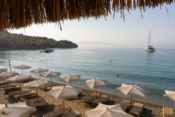 Sunbeds and rattan parasols on beach. Beautiful empty beach with sun umbrellas and sunbeds. Straw sunshades and sunbeds on the empty beach with blue sea on background.
