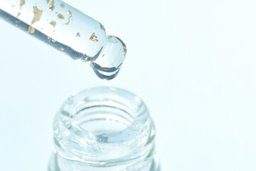 Serum gel texture swatch. Transparent drop with golden sparkles. Blue background. Face skincare product. Liquid oil essence. Beauty collagen splash. Organic peeling treatment. Body health care