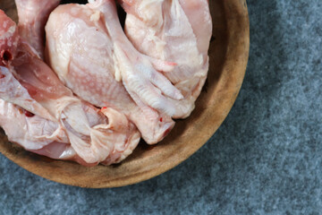 Pieces of raw chicken on a wooden plate on gray background