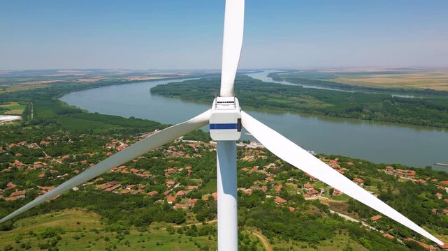 Aerial close up footage of operational wind turbine generator. Flying around rotors and blades at a windfarmwith beautiful landscape. Alternative energy on a warm summer day. Green electricity.
