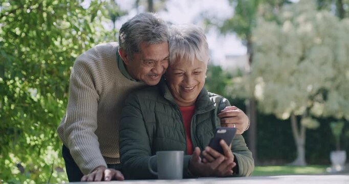 Happy, loving and mature old couple in love on phone video call outdoors in nature home garden. Smiling husband hugging and kissing wife while they laugh at funny graphic or meme on social media.