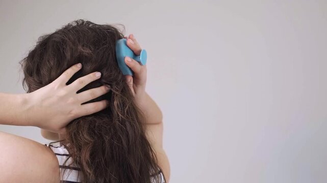 Portrait of a beautiful young girl with long dark hair, applying hair growth oil with a pipette, and massaging her scalp with a brush.