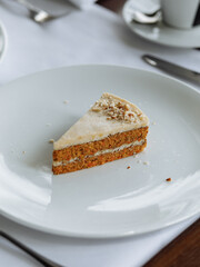 delicious cake with white buttercream, white sponge layers, and fresh nuts, served on a beautiful white plate on a wooden table in a cozy, charming restaurant