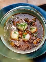 delicious, rich soup with juicy beef, fresh vegetables, and fragrant herbs, served in a beautiful blue bowl on a wooden table in a cozy, charming restaurant