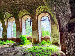 Fototapeta premium Light filters through arched windows illuminating the overgrown interior of an abandoned brick structure
