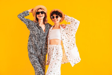 Two young beautiful smiling brunette hipster female in trendy summer clothes. Sexy women posing near yellow wall in studio. Positive models having fun. Cheerful and happy