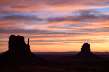Breathtaking view of the Monument Valley Mittens in Arizona during dusk. The silhouette of the rock buttes against the colorful pink and orange sky creates a beautiful sunset atmosphere - USA