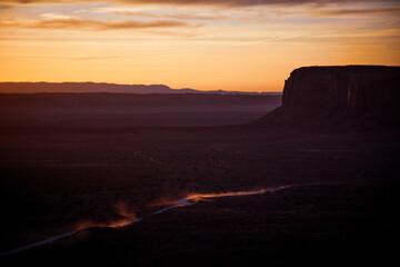 Breathtaking view of Monument Valley at dawn, featuring a dusty road winding through the landscape. Captured in Arizona, USA, the scene highlights the beauty and silhouettes of this iconic location.