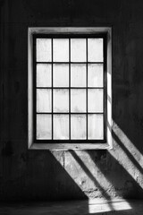 Obraz premium A window in a black-and-white industrial loft, with sharp sunlight casting dramatic shadows on concrete walls. 