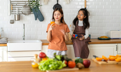 Portrait of enjoy happy love asian family mother with little asian girl preparing drinking glass of fresh juice and orange on counter in kitchen at home.Diet concept.healthy drink.
