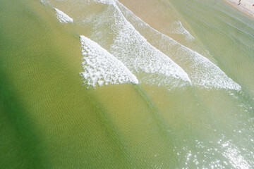 zenithal drone photograph of turquoise sea water and surf foam near the shore, textured background