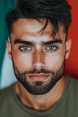 Fototapeta premium Close-up photo of an attractive man with short black hair, blue eyes, and a beard, looking at the camera directly, with the Italian flag in the background.
