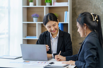 Two young businesswomen are analyzing data and working together on a project using a laptop in the office