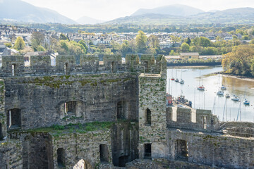 a line of moored yachts in an estuary beyond stone walls of Caernarfon Castle, a medieval fortress...