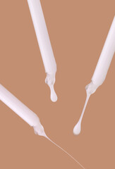 pipettes with white serum close-up falling drops on a beige background