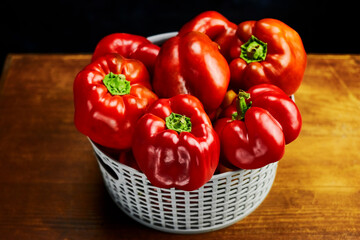 still life, gray mesh basket with several red bell peppers close-up, cozy vibe, natural product, dark background, wooden table