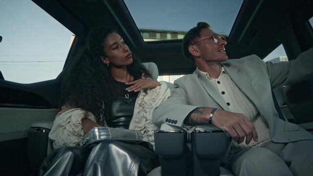 Medium shot of interracial celebrity couple wearing fancy outfits shooting ugc for social media on smartphone in backseat of luxury car and paparazzi taking pictures of them through window