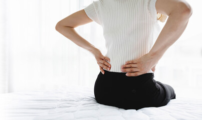 Woman holding her lower back while sitting in bed has chronic back pain. Health Care concept