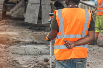 Construction worker using surveying equipment on busy job site during daytime